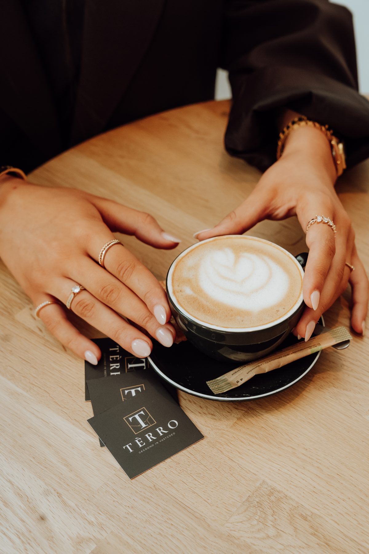 Handen rond een kop koffie naast TÈRRO-visitekaartjes